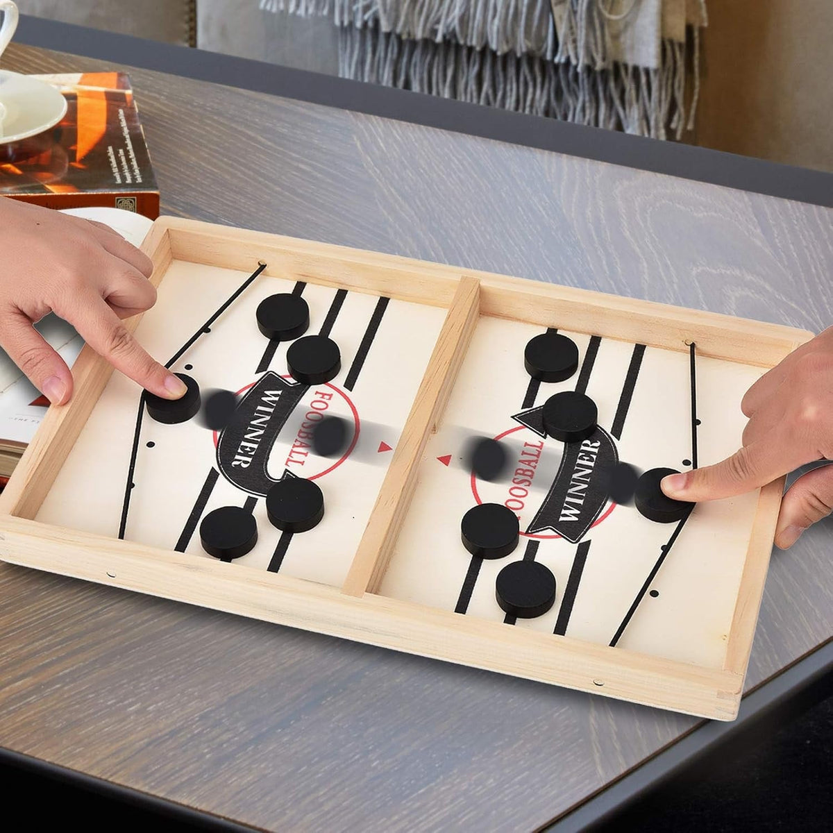 Two players flicking pucks through the gap in a wooden slingshot table game