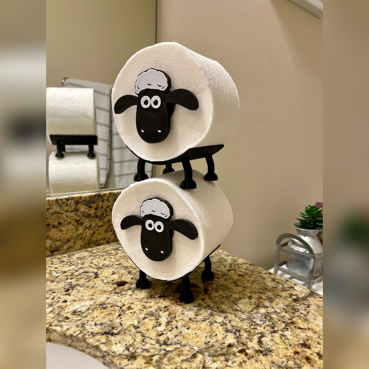 Two stacked sheep toilet roll holders beside a bathroom mirror